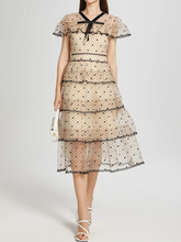 Woman wearing a tiered lace dress with a plain background